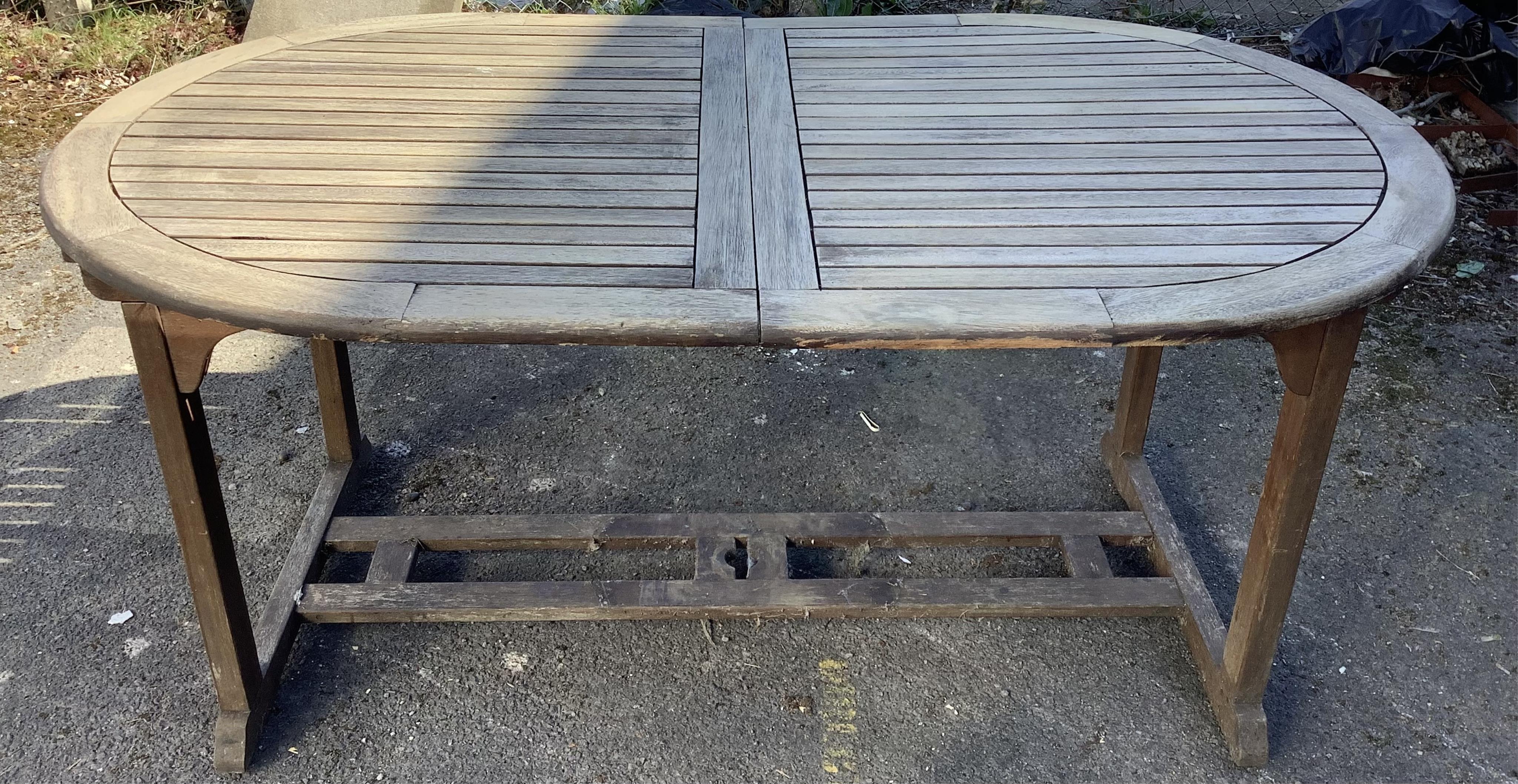A weathered oval teak extending garden table, width 230cm extended, depth 102cm, height 77cm and six weathered teak folding garden chairs. Condition - fair